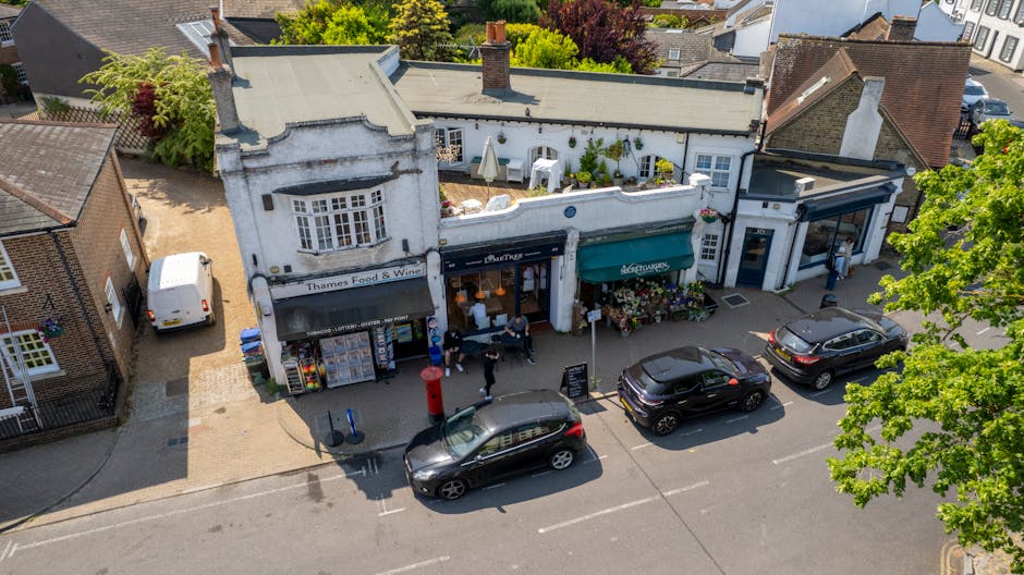 An aerial view of a small shopping street featuring a white, semi-detached building with a black awning labeled 'Thames Food & Wine' and a green awning with the Gardeners Harrow on the Hill logo. The 